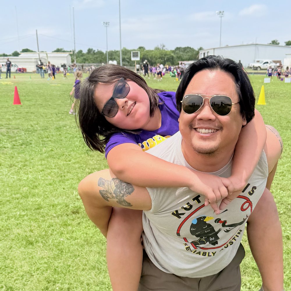 Lincoln riding piggyback on her dad at field day